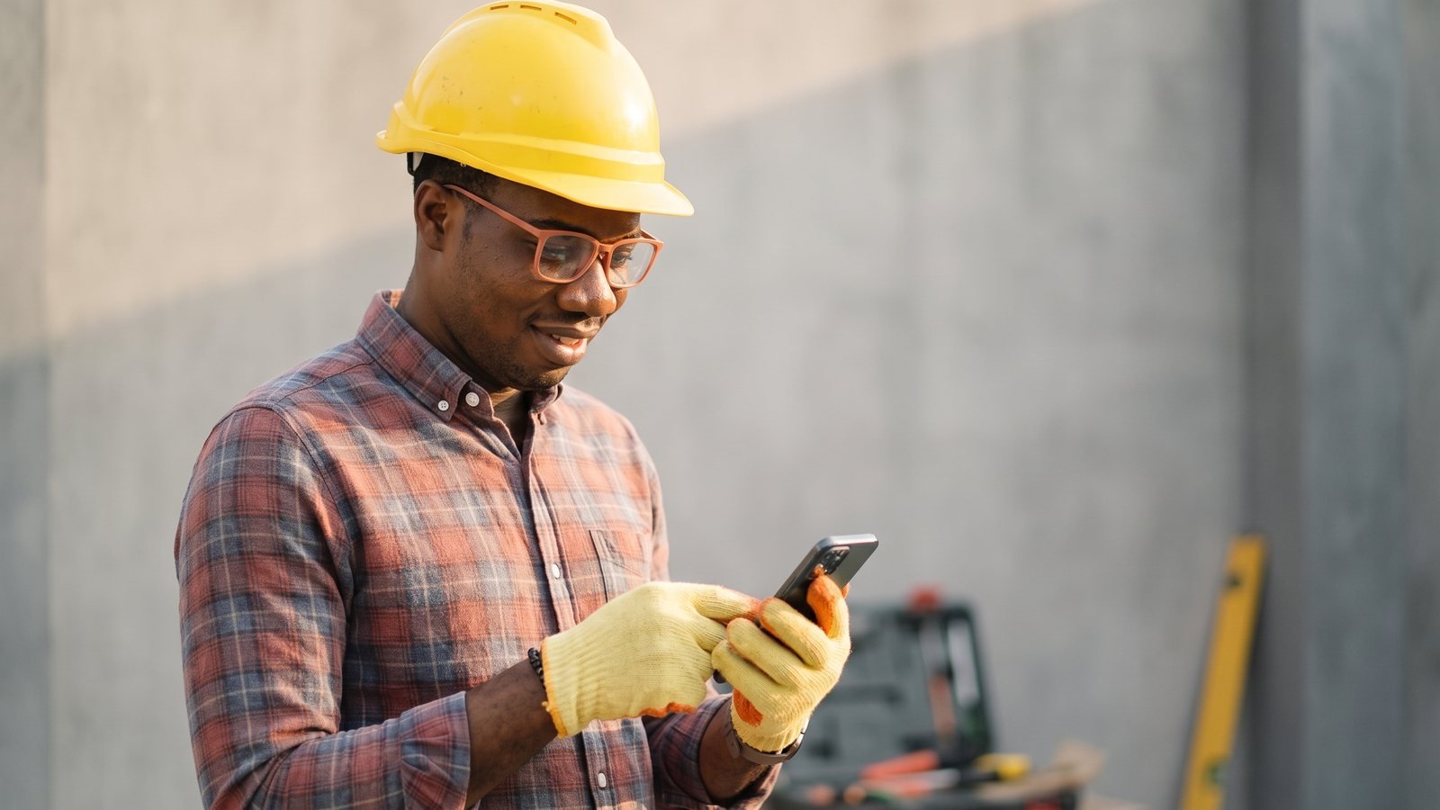 Artisan plombier consultant son téléphone sur un chantier, casque de chantier posé à côté d'une caisse à outils